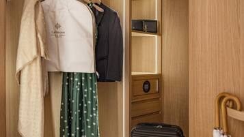 A hotel room with a wooden wardrobe, a suitcase, and a coat rack with clothes and a hat.