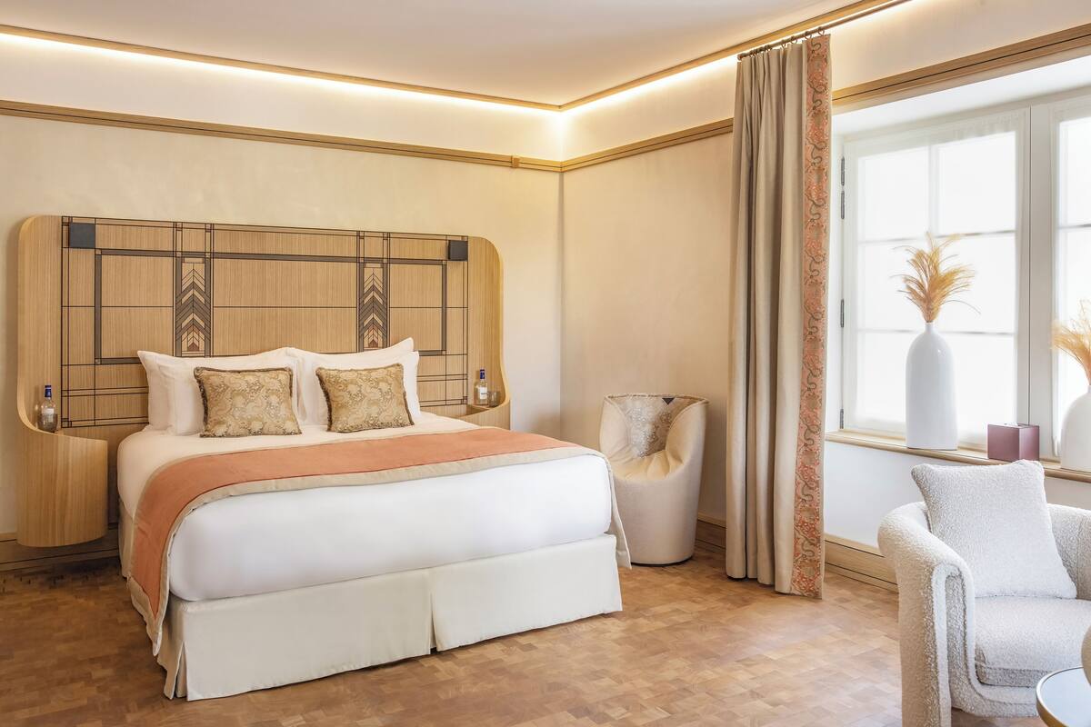 Une chambre à coucher moderne avec un grand lit, une table de chevet, une chaise et une fenêtre avec des rideaux.