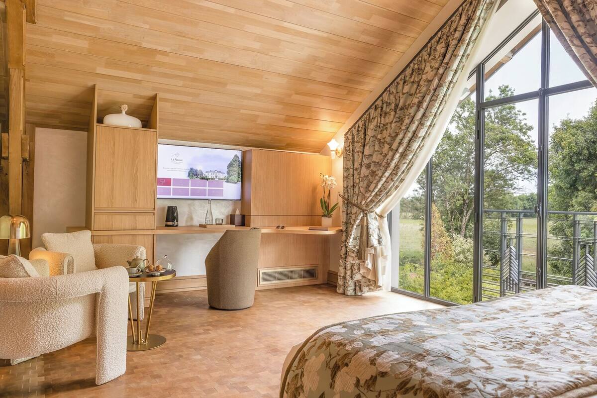 Une chambre confortable avec un grand lit, un bureau en bois, un fauteuil confortable et un téléviseur diffusant un paysage pittoresque.