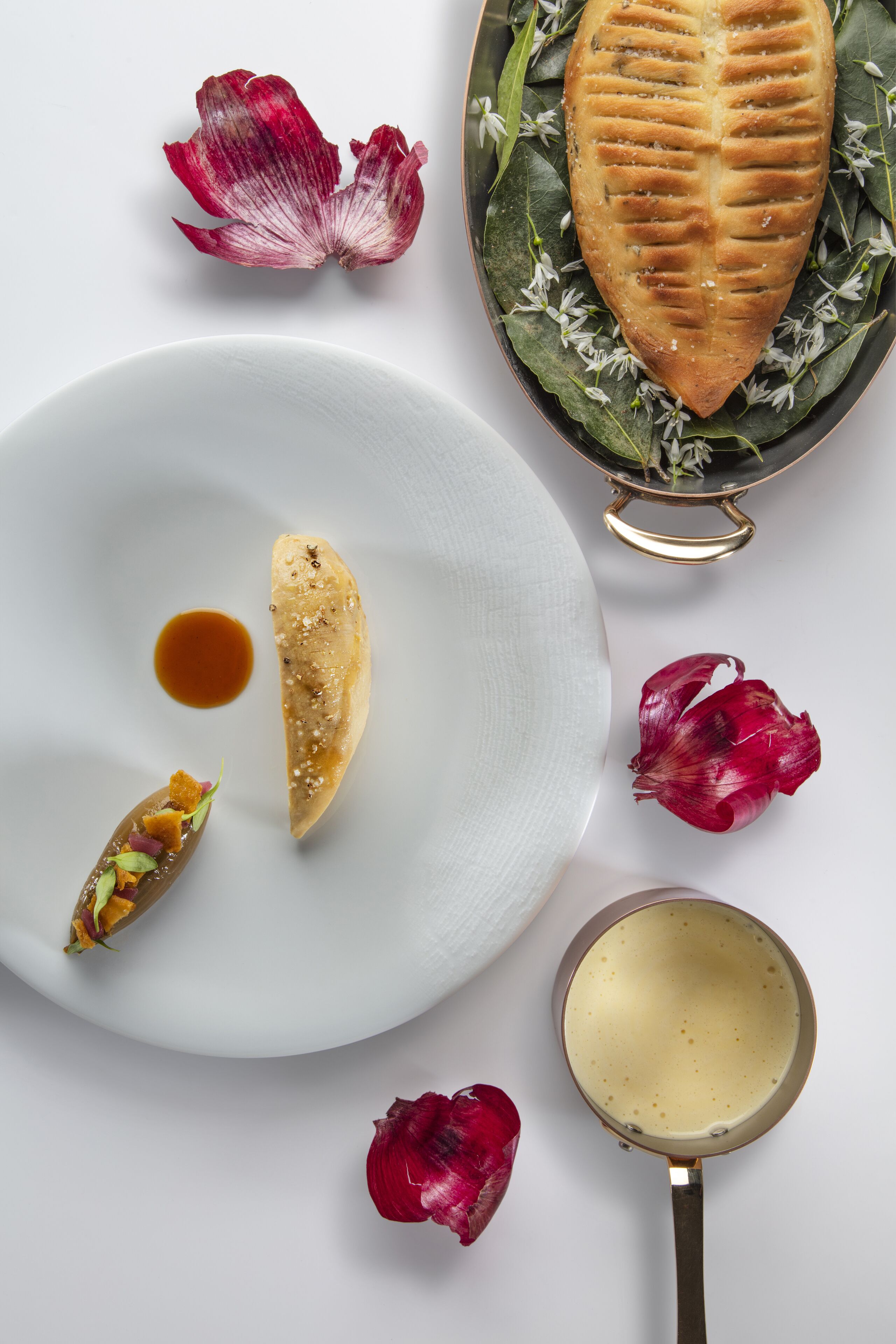 Un plato blanco con un pastel, un tazón pequeño de salsa y un recipiente metálico con una crema.