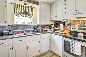 Una cocina con armarios blancos, encimera de granito, un lavabo, una estufa y diversos utensilios de cocina.
