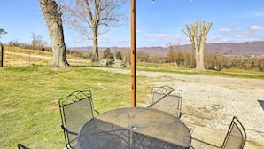 A patio with a round table and metal chairs, surrounded by trees and a clear view of distant mountains. - Farmhouse: Close to Norris Lake & ATV Trails! (LaFollette)