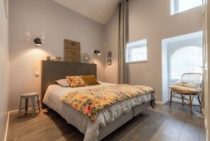 Ein Schlafzimmer mit einem Bett, einem Sessel, einem kleinen Hocker und einem Fenster.