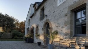 Un bâtiment en pierre avec une allée gravillonnée, un banc et des plantes en pot.