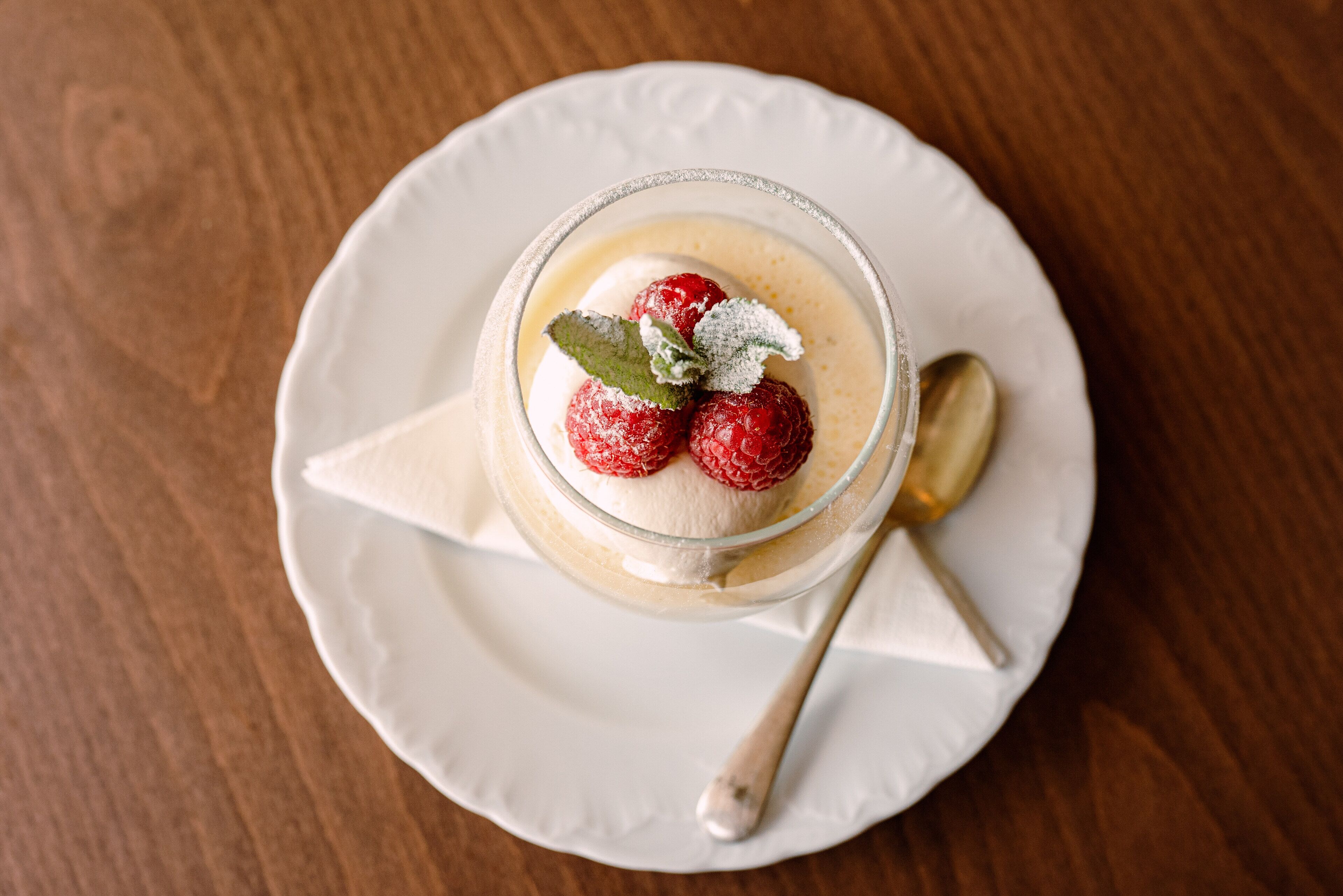 A dessert in a glass on a white plate with a spoon.