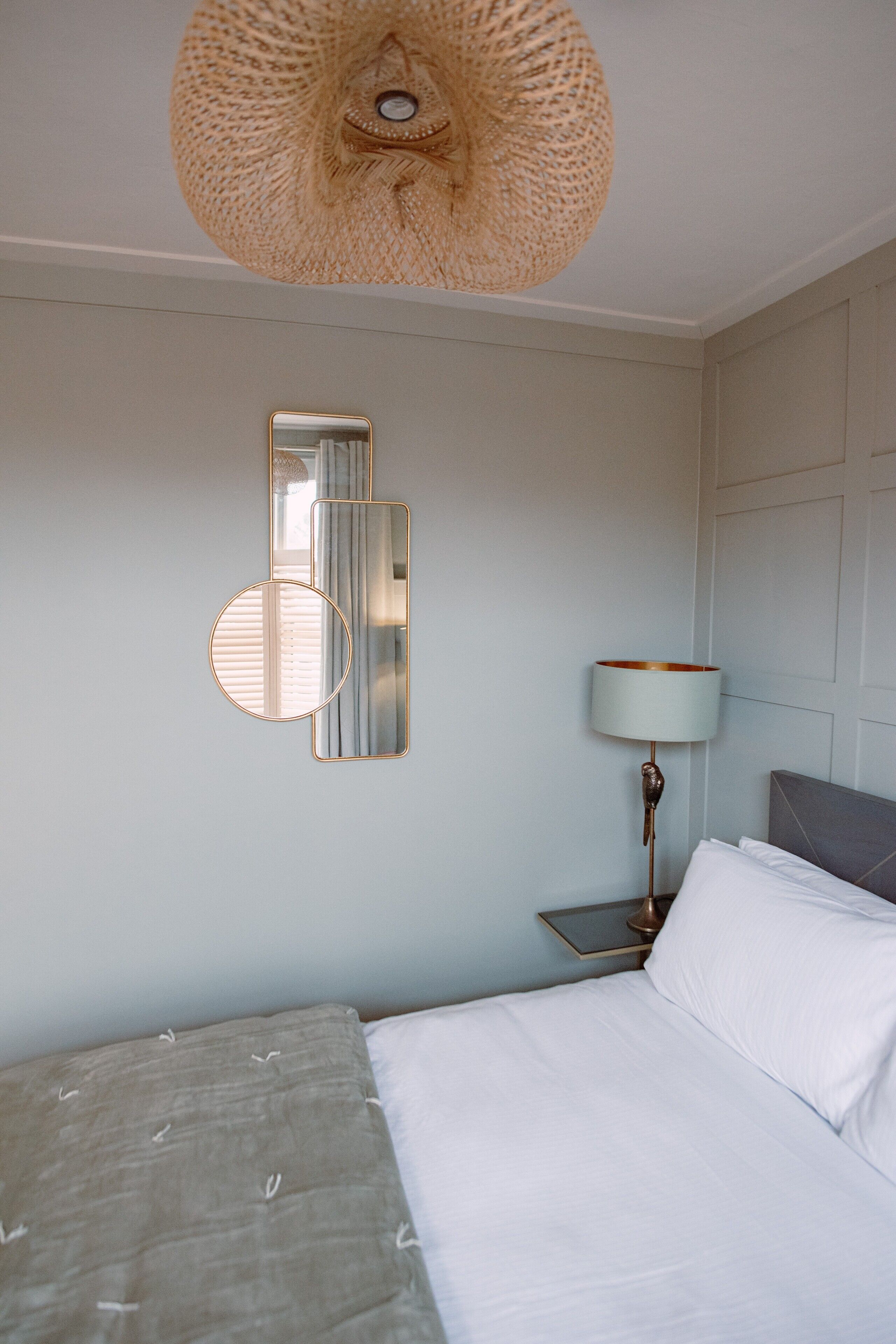 A bedroom with a bed, a nightstand, a lamp, and wall-mounted mirrors.
