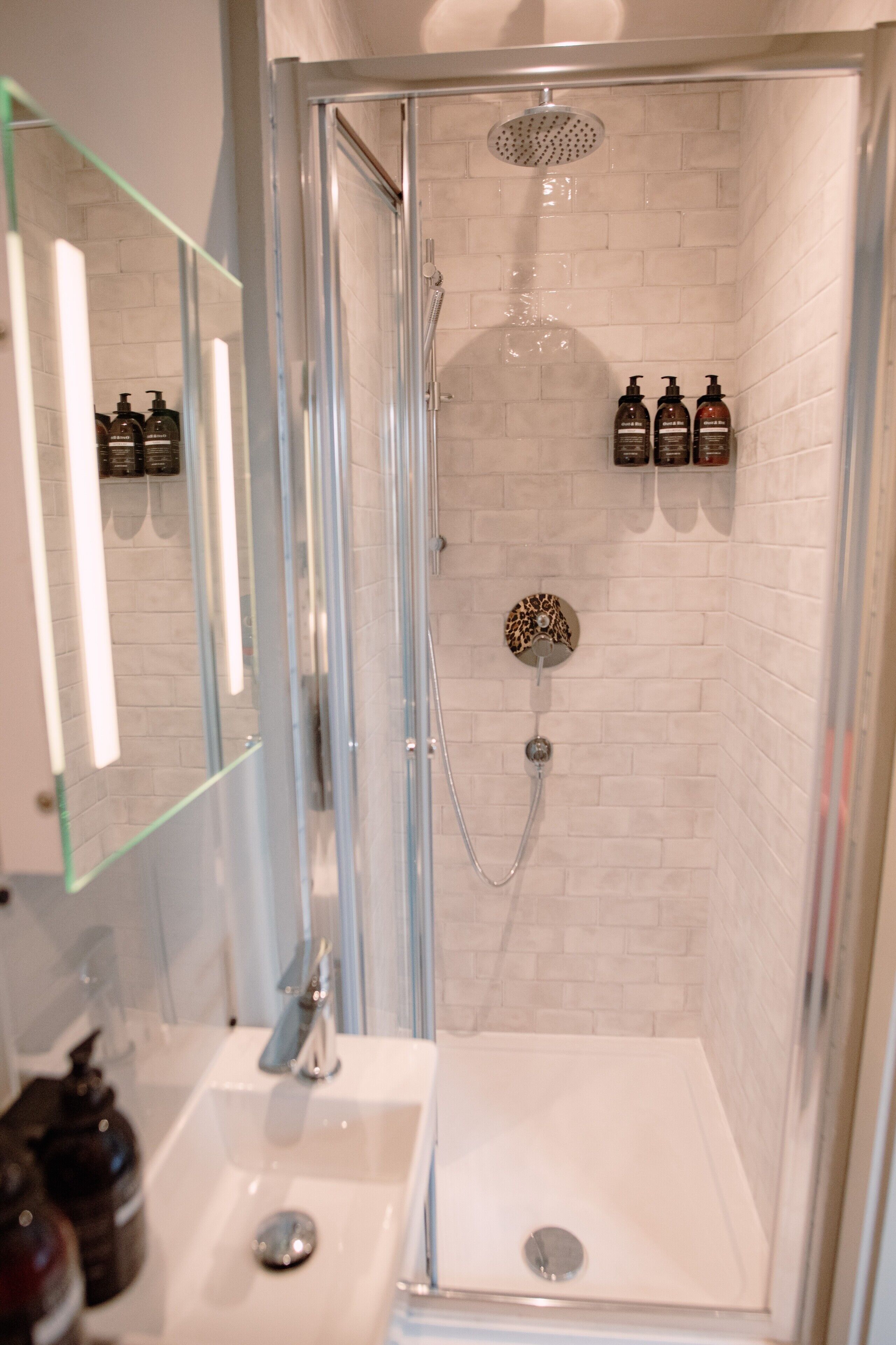 A modern bathroom with a glass-enclosed shower, white tiled walls, and a mirror above the sink.