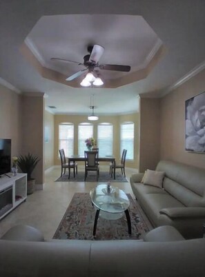 Relax in this spacious living room with a high ceiling, featuring a sofa, coffee table, dining area, and TV.