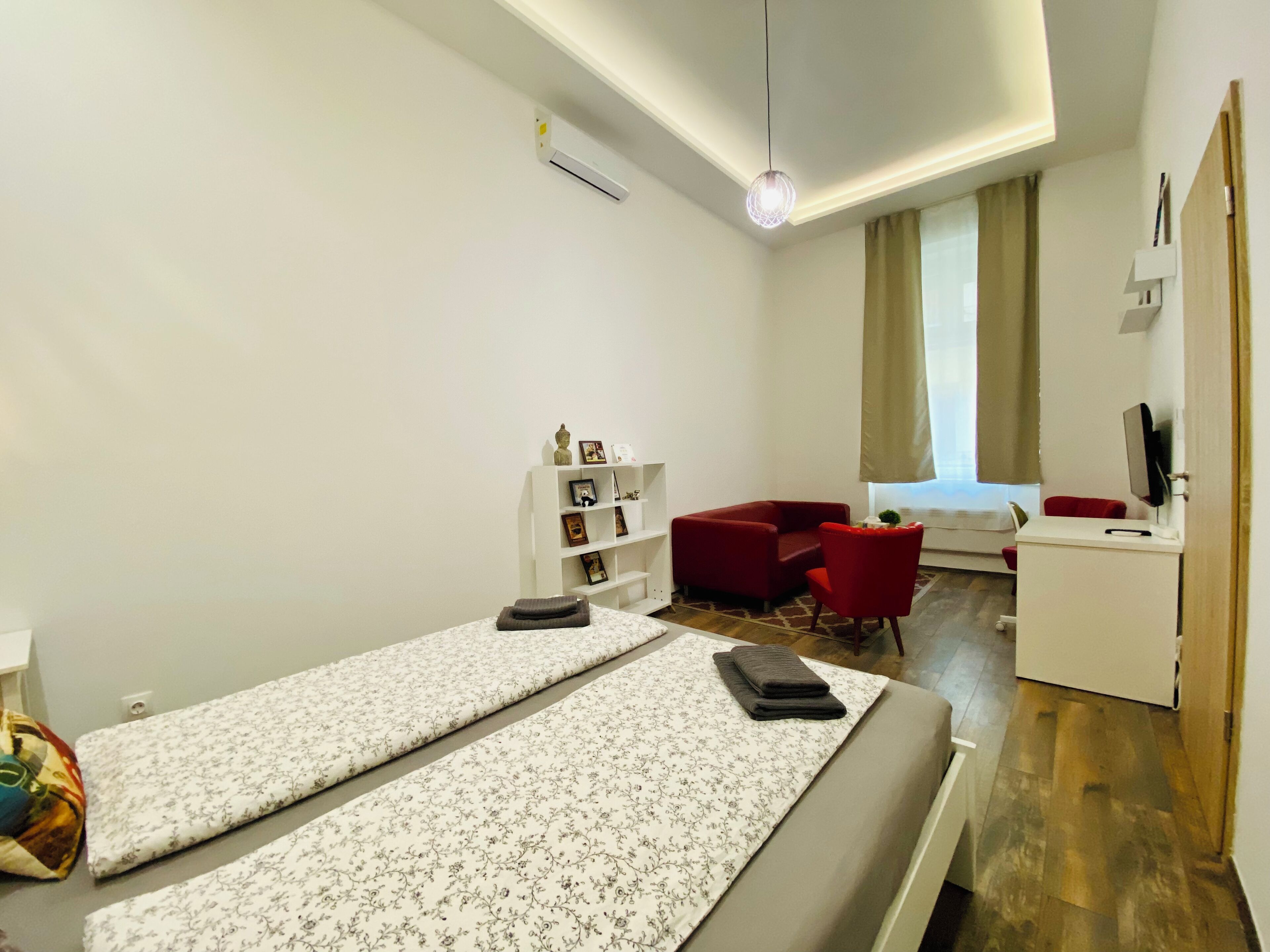 A modern hotel room with a bed, a desk, a chair, a small sofa, and a TV.