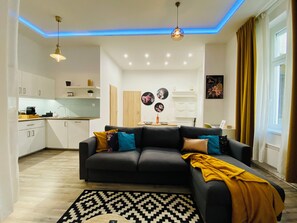 A modern living room with a grey sofa, a patterned rug, and a kitchen in the background. - Chic Luxury Central Studio with A/C - Tropical House (Budapest)
