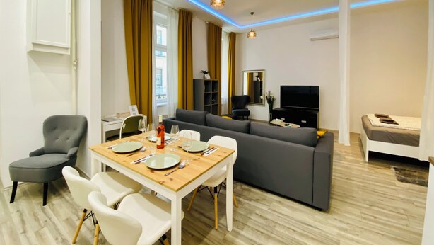 Ein modernes Wohnzimmer mit einer Couch, einem Esstisch für vier Personen und einem Fernseher.