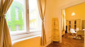 A room with a radiator, a window with curtains, a wooden herringbone floor, and a dining area with chairs and a table. - Large Peaceful 1BR Central Apt A/C - Yellow House (Budapest)