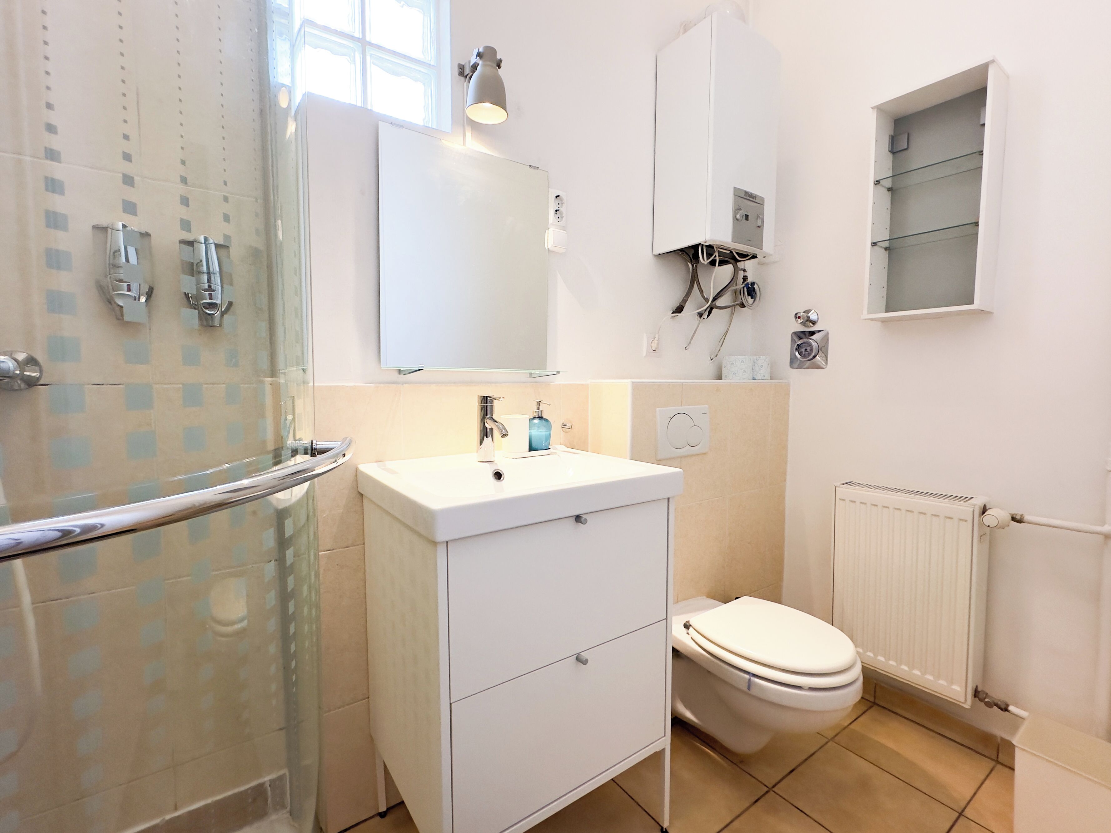 Un baño moderno con cabina de ducha de vidrio, un lavabo blanco con espejo, un inodoro y un radiador.