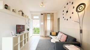 A modern living room with a sofa, a TV, a wall clock, and a bookshelf.