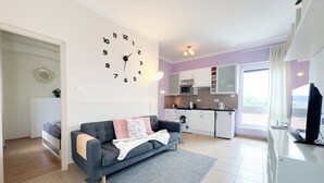 Una sala de estar moderna con un sofá gris, un reloj de pared grande y una zona de cocina con microondas y lavadora.