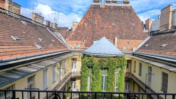 A courtyard with a central building featuring a conical roof and ivy-covered walls, surrounded by buildings with red-tiled roofs.