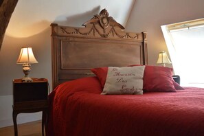 Un dormitorio con cabecera de madera, colcha roja y almohada con texto. Hay dos mesitas de noche con lámparas.