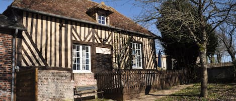 A traditional half-timbered house with a brick foundation, wooden beams, and a thatched roof.