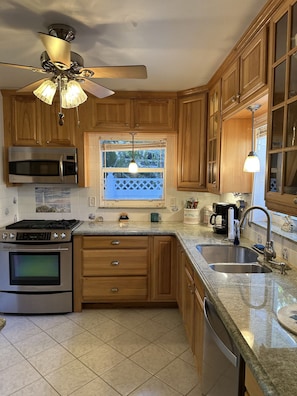A kitchen with wooden cabinets, a built-in microwave, a stove, a window with a view, and a ceiling fan.