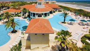 A resort with a central building, multiple swimming pools, and a beach view.