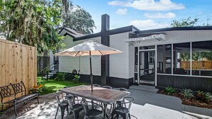An outdoor patio with a wooden table and chairs, a metal bench, and a large umbrella.