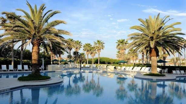A swimming pool surrounded by palm trees and lounge chairs.