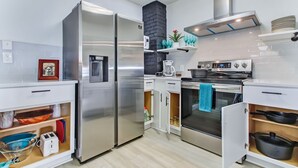 A modern kitchen with stainless steel appliances, white cabinetry, and a black brick accent wall.