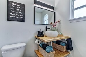 Une salle de bain comprenant des toilettes, un lavabo avec un miroir, un panneau noir, une fenêtre et des paniers de rangement.