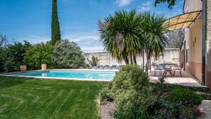 A swimming pool with a lawn, a tall tree, and a patio area with chairs and a table.