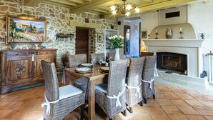 A rustic dining area with stone walls, wooden beams, and a fireplace.