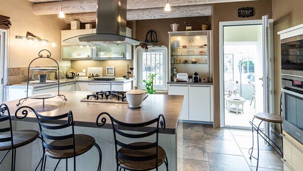 A modern kitchen with a central island, bar stools, a large stove, and a built-in oven.