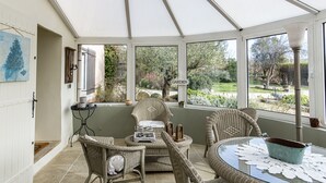A conservatory with wicker furniture, a glass table, and a view of a garden.
