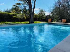 Une piscine rectangulaire à l’eau d’un bleu limpide, entourée d’une pelouse bien entretenue et d’arbres.