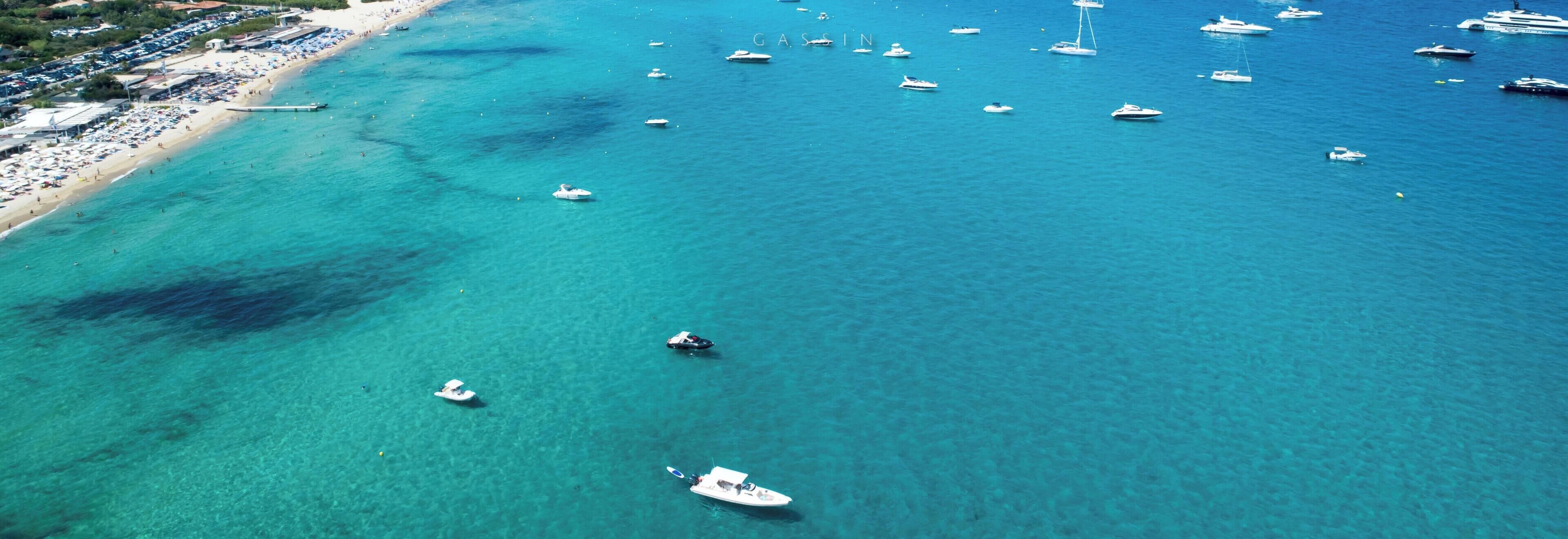 An aerial view of a coastal area with a beach, boats, and a mountainous backdrop.