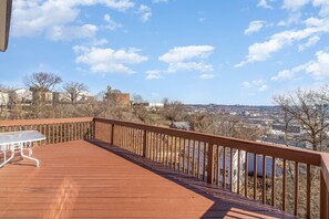 A wooden deck with a metal table, overlooking a town with buildings and trees. - Downtown Cincinnati Views—Prime Location, A Few Minutes to Everything! (Cincinnati)