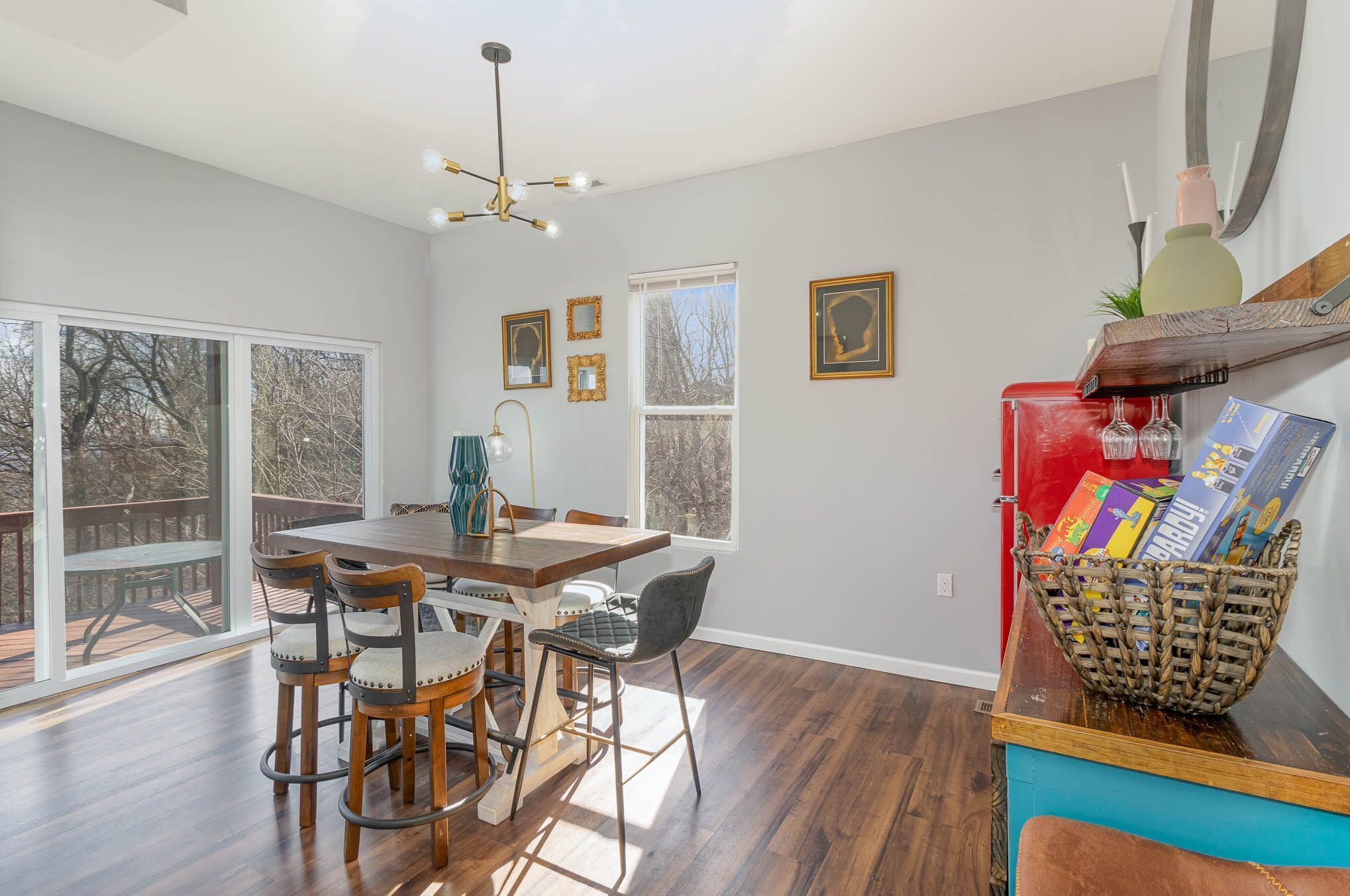 A dining area with a wooden table and chairs, large windows, and a ceiling light fixture.