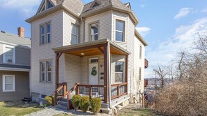Une maison à deux étages avec un porche à l’avant, un petit jardin devant et une porte d’entrée bien visible.