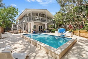 A two-story house with a pool, outdoor furniture, and a wooden deck.