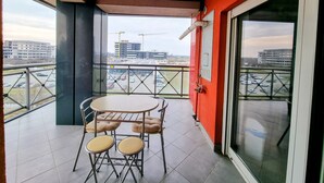 Un balcon avec une table et des chaises, donnant sur un parking, avec des bâtiments en arrière-plan.