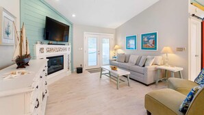 A living room with a fireplace, a sofa, a television, and artwork on the walls. - Island Sun House - Walk to State Park and Beach! (St. Augustine)