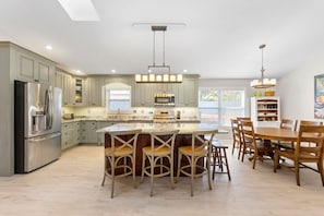 A spacious kitchen with a central island, wooden chairs, and a dining table.