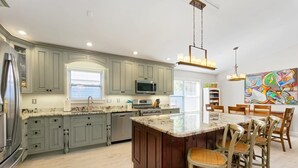 A modern kitchen with a large island, built-in appliances, and a dining area with chairs. - Island Sun House - Walk to State Park and Beach! (St. Augustine)