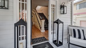 A white wooden exterior with a black and white striped cushion, a black lantern, and a welcome mat at the entrance. - The Gatsby Mansion/Heated Pool/Heart of Town (St. Augustine)