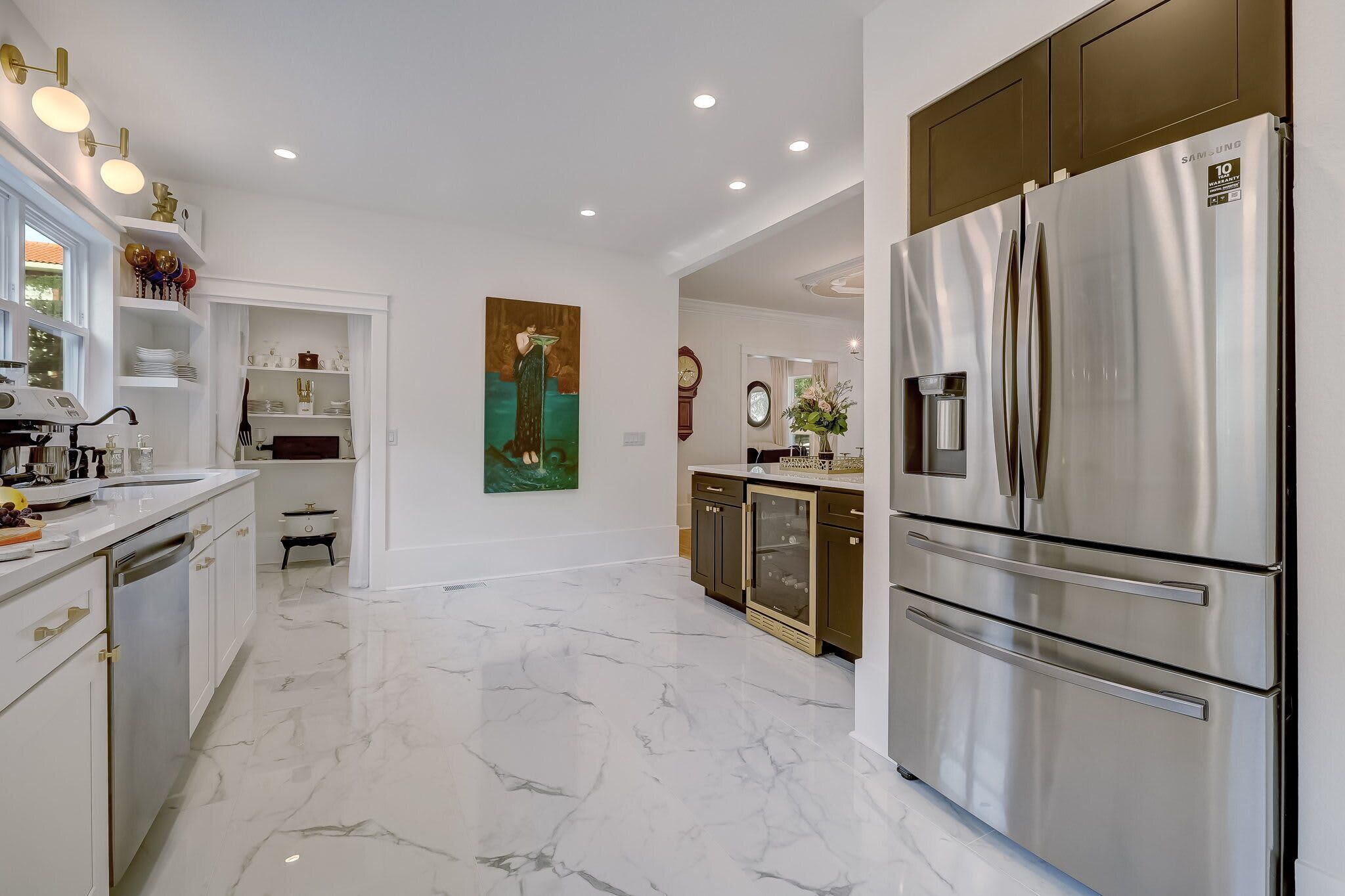 A modern kitchen with a stainless steel refrigerator, marble flooring, and a painting on the wall.