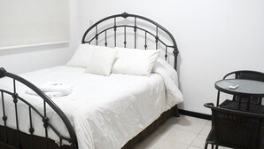 Un lit simple avec un cadre en métal, une petite table ronde et une chaise.