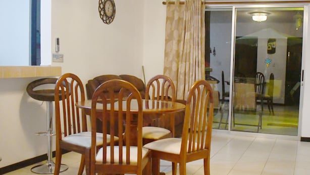 Un coin repas avec une table ronde et six chaises en bois, un petit tabouret de bar et une horloge murale.