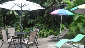 Un espace extérieur aménagé avec une table ronde et quatre chaises, entouré de parasols et d’une végétation luxuriante.