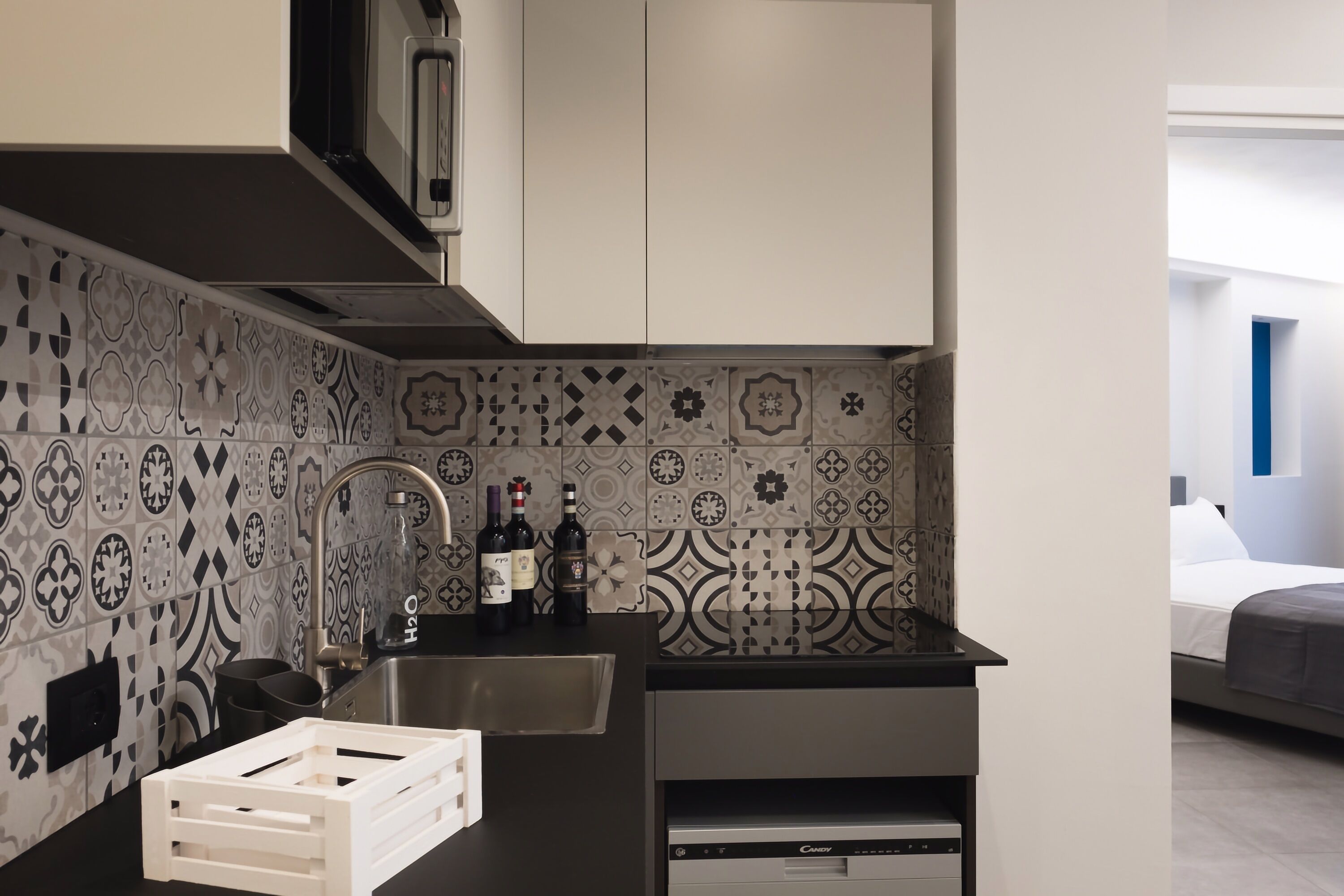 A compact kitchen with a sink, microwave, and wine bottles.