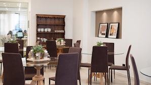 Een moderne eethoek met ronde glazen tafels en bruine stoelen, een houten boekenkast en lijstwerken aan de muur.