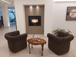 A modern living room with a fireplace, two brown armchairs, and a small wooden table with decorative items.